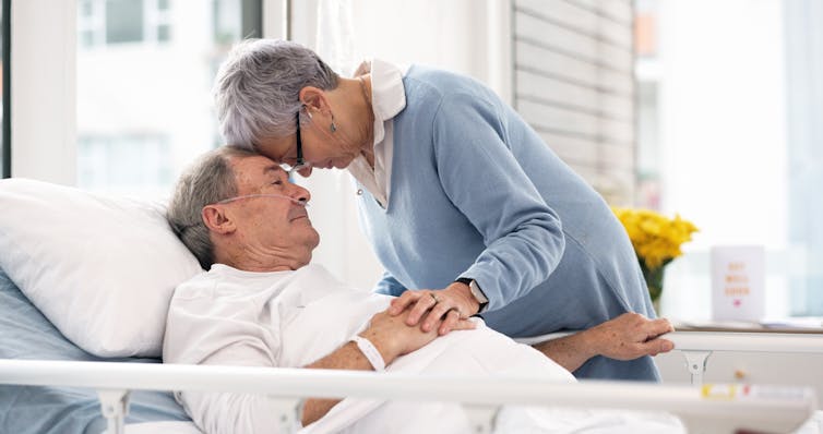 A couple puts their heads together in the hospital. The person is lying down, and has a breathing support device attached to the nose.